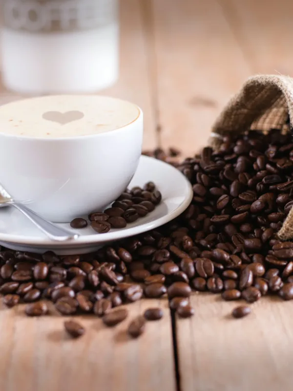 Φλιτζάνι καφέ σε τραπέζι καφετέριας, με φόντο τιμοκατάλογο και έκφραση προβληματισμού καταναλωτή.